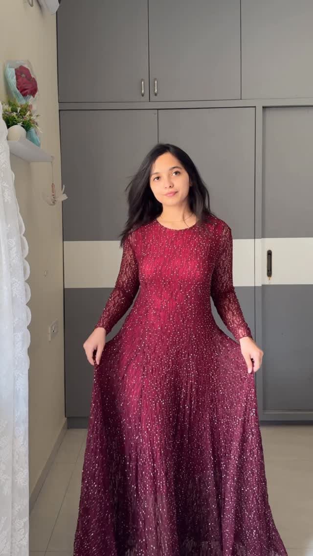 Woman wearing a sparkling burgundy long-sleeved A-line gown in a home setting.