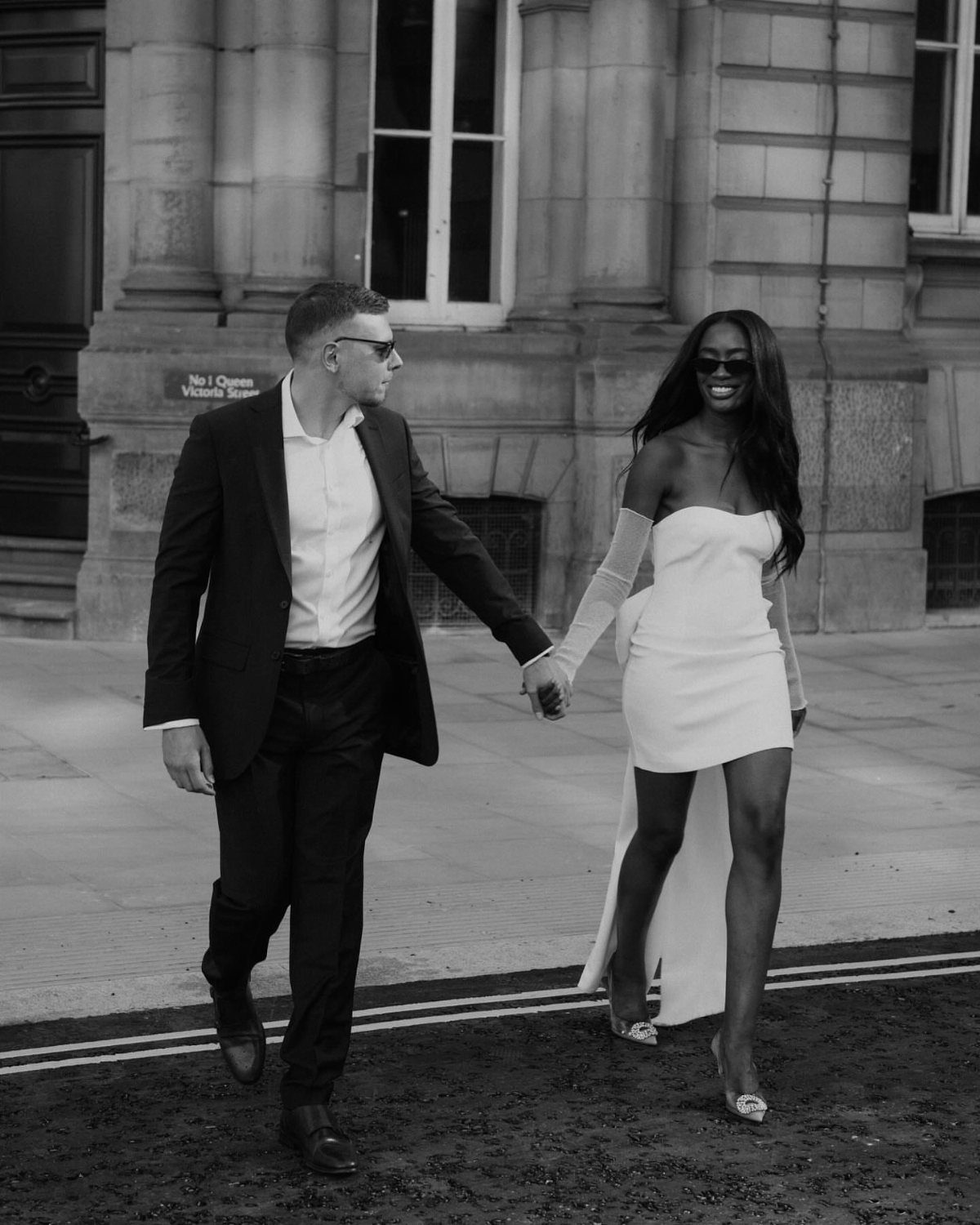 Couple walking in city, woman wearing a sleek white modern dress with long train.