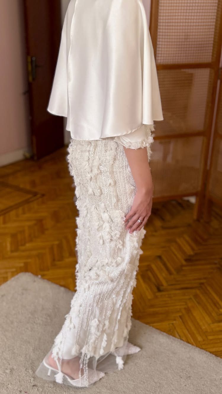 White textured gown with a smooth satin capelet and white high-heeled sandals.