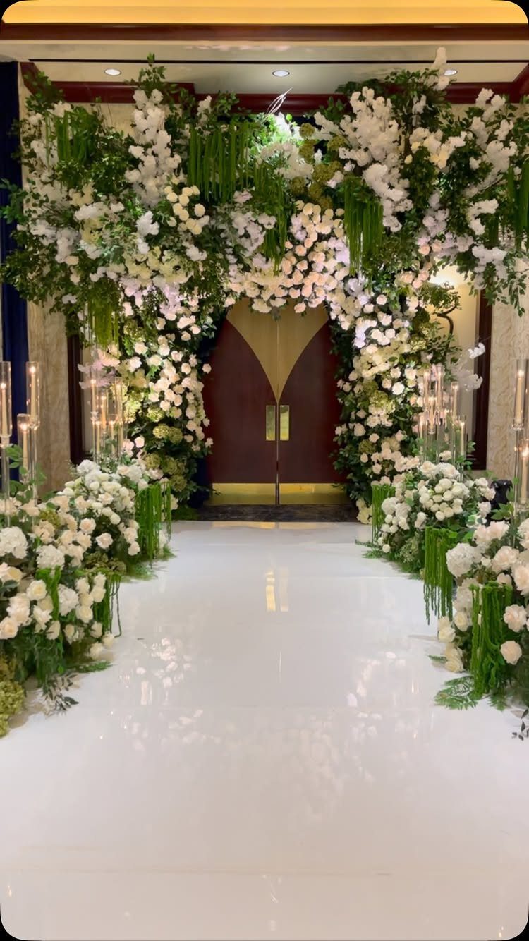 9 Fall Floral Wedding Ideas for Rich Color and Texture 8 White floral clusters and tall candles line a bright white aisle leading to a floral arch.