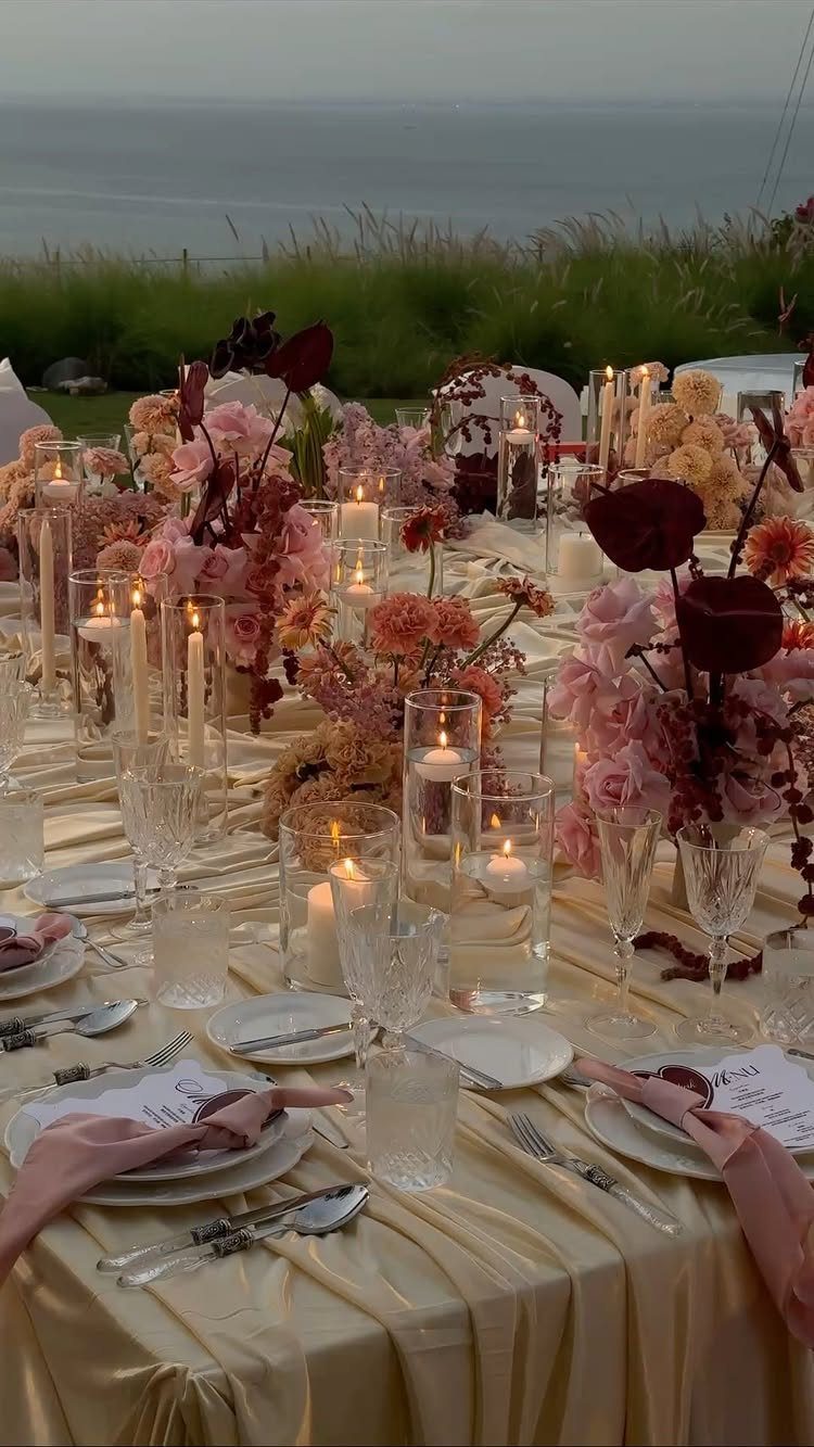 9 Fall Floral Wedding Ideas for Rich Color and Texture 2 A decorated wedding table with gold linens, lit candles, and pink and burgundy floral arrangements.