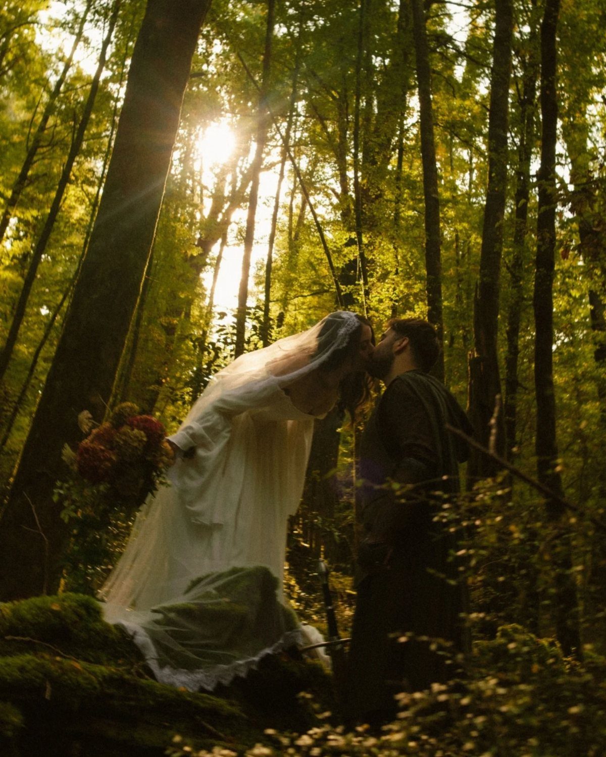 Fantasy Inspired Wedding: 9 Ideas from Forest Photos to Celestial Lace 9 A bride and groom kissing in a sunlit, magical forest setting during a wedding.