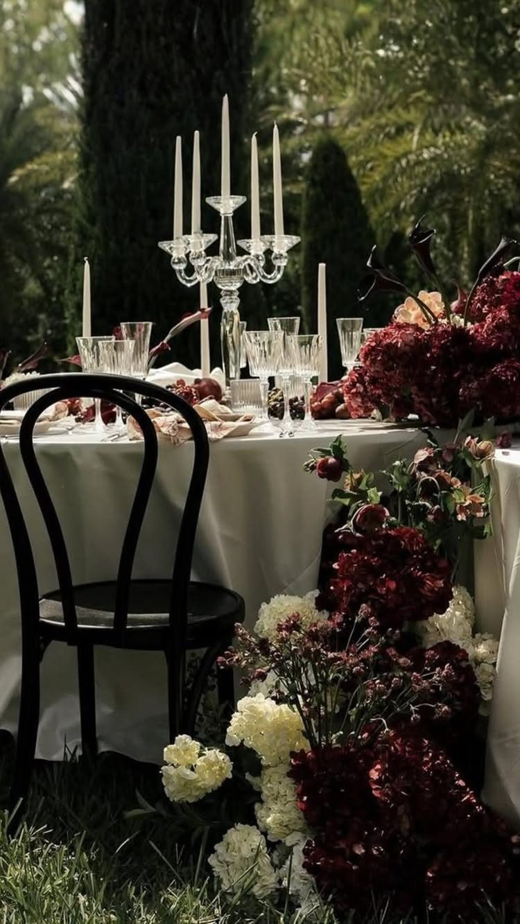 Fantasy Wedding Ideas: 9 Decor, Attire and Theme Details for 2026 4 A formal outdoor table set with dark red flowers, white candles, and a black chair.