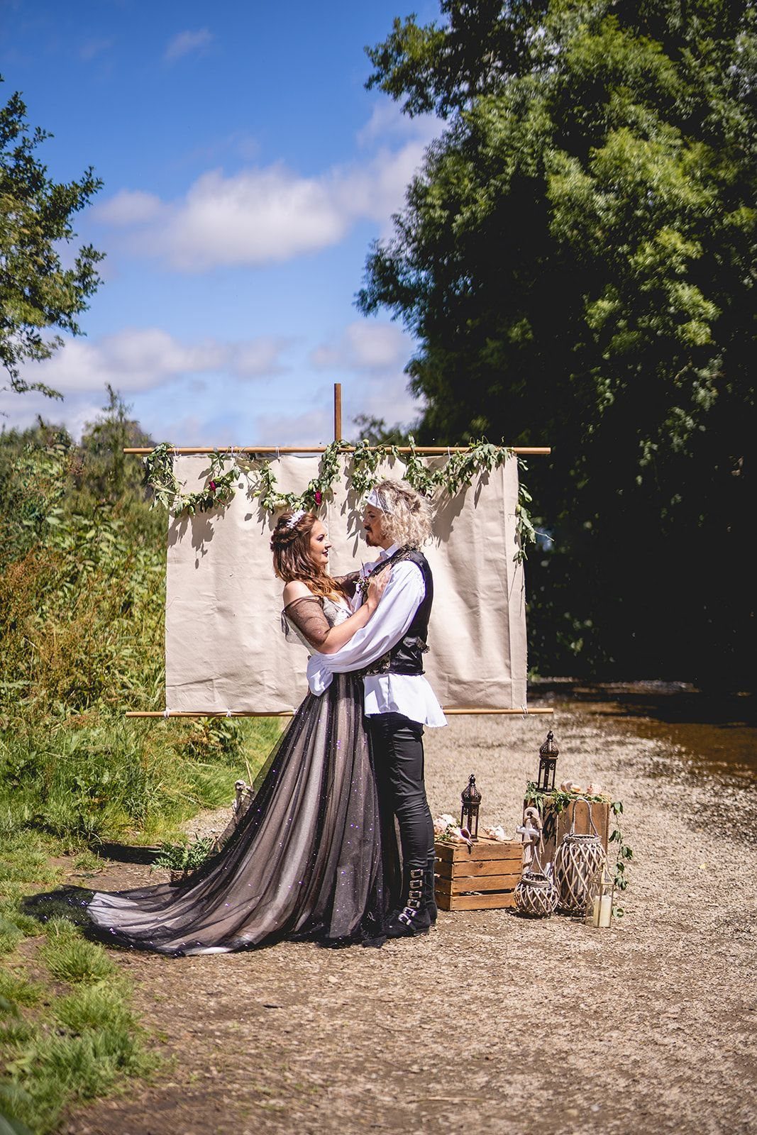 Fantasy Wedding Ideas: 9 Decor, Attire and Theme Details for 2026 10 A couple in fantasy wedding attire embracing in front of a fabric backdrop outdoors.
