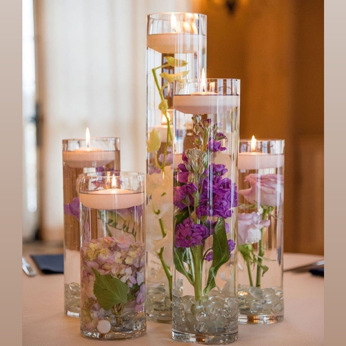 Flower Wedding Decor: 8 Ideas for Ceremony and Reception 2 Tall glass vases containing floating candles and colorful flowers arranged on a table.