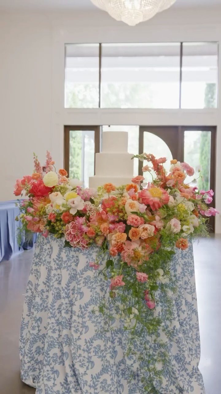 Flower Wedding Decor: 8 Ideas for Ceremony and Reception 9 A white wedding cake on a patterned table surrounded by lush pink and orange floral arrangements.