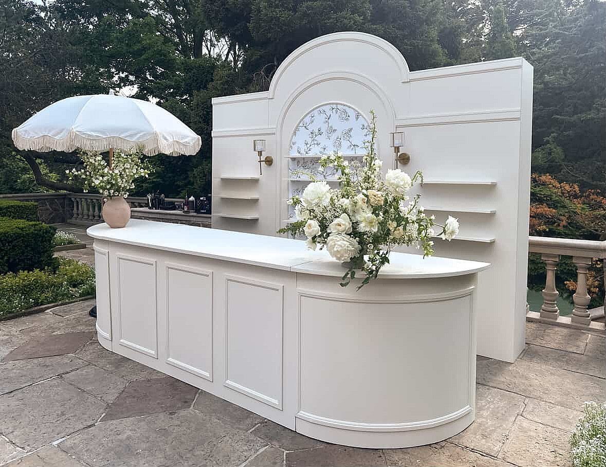 Flowers for Wedding Reception: 11 Elegant Ideas to Style Your Space 4 White outdoor wedding bar with elegant white floral arrangements and a white umbrella.