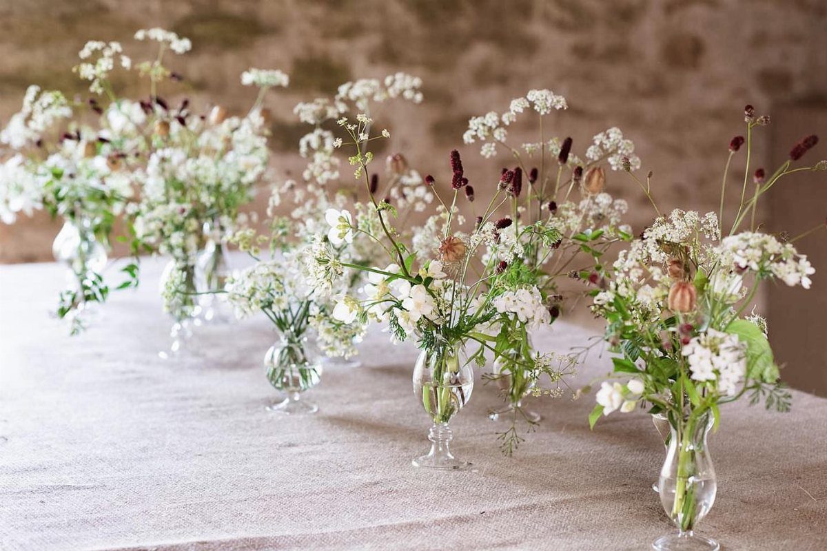 Flowers for Wedding Reception: 11 Elegant Ideas to Style Your Space 9 Small glass bud vases with white and purple flowers on a linen table.