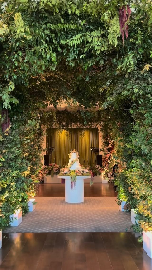 19 Forest Theme Wedding Decorations From Greenery Canopies to Candlelit Paths 13 Lush green foliage archway framing a white wedding cake on a pedestal.