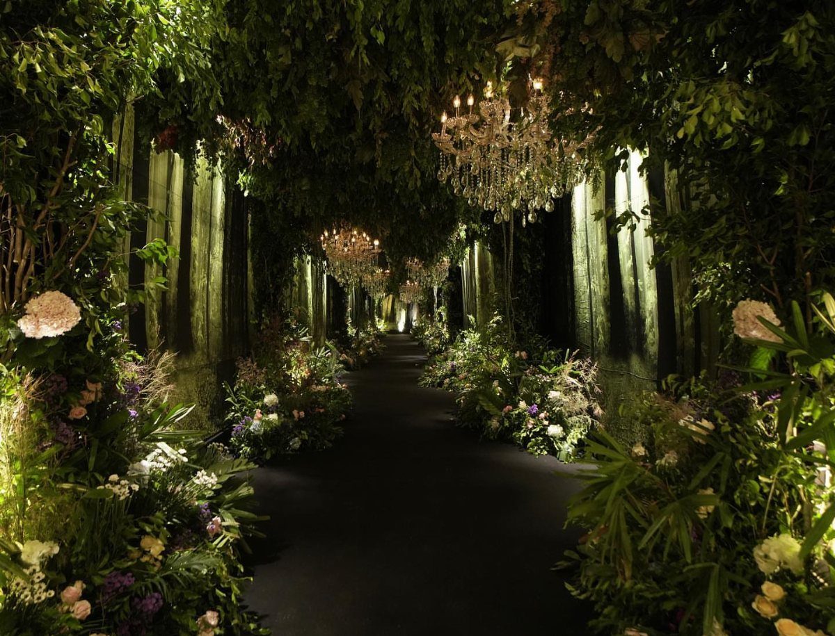 19 Forest Theme Wedding Decorations From Greenery Canopies to Candlelit Paths 16 A dark, flower-lined pathway under a canopy of greenery with hanging crystal chandeliers.