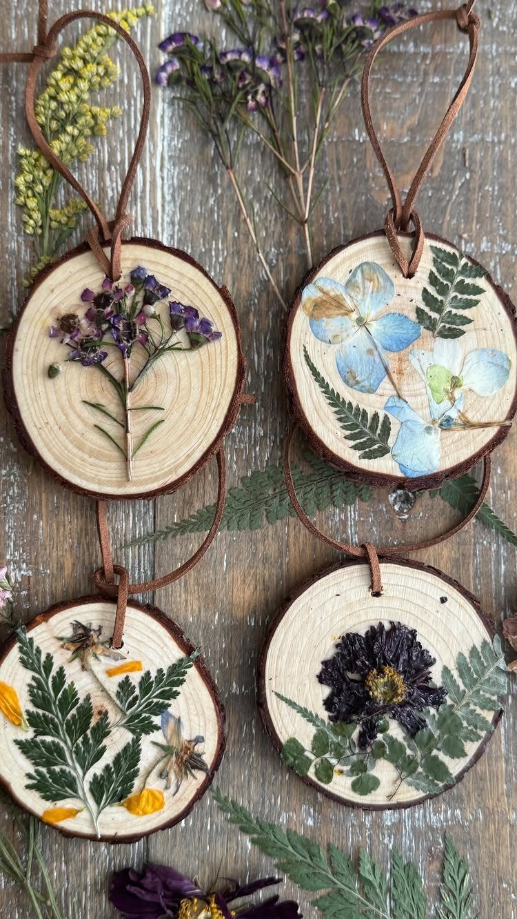19 Forest Theme Wedding Decorations From Greenery Canopies to Candlelit Paths 18 Four wood slice ornaments featuring pressed dried flowers and greenery hanging on a rustic wooden surface.
