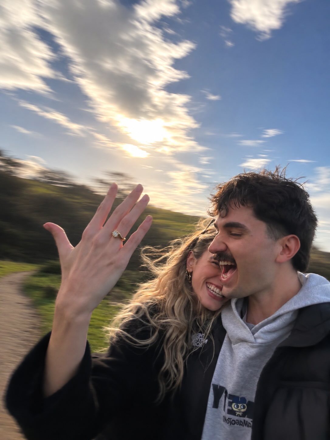 7 Funny Save the Date Ideas That Skip the Boring Part 7 Smiling couple outdoors with woman showing engagement ring and man making a funny face.