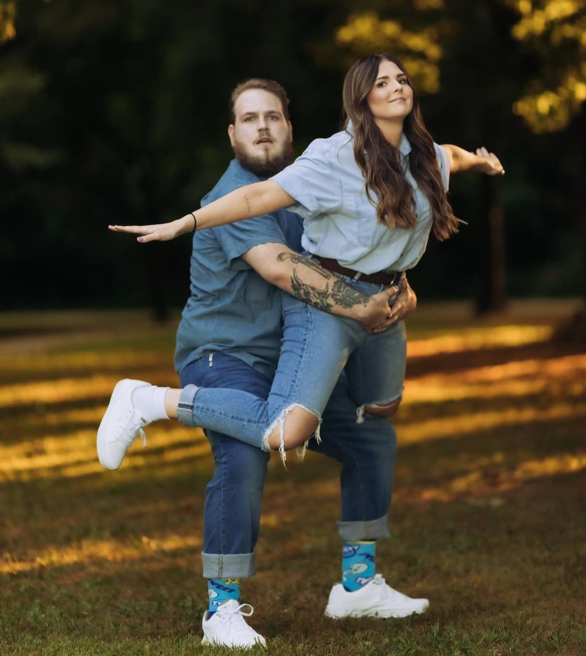 7 Funny Save the Date Ideas That Skip the Boring Part 8 Man holding a woman in a playful airplane pose outdoors in a grassy field.