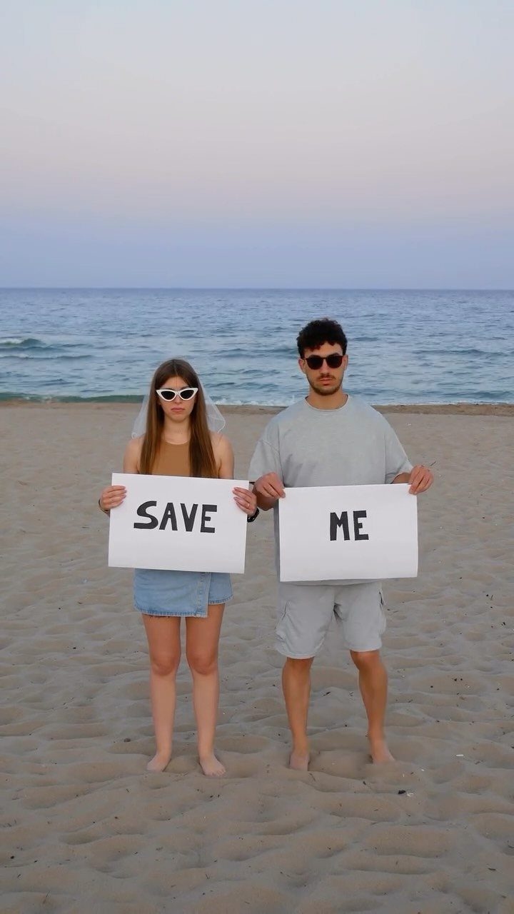 7 Funny Save the Date Ideas That Skip the Boring Part 5 Couple on a beach holding signs that together read SAVE ME.