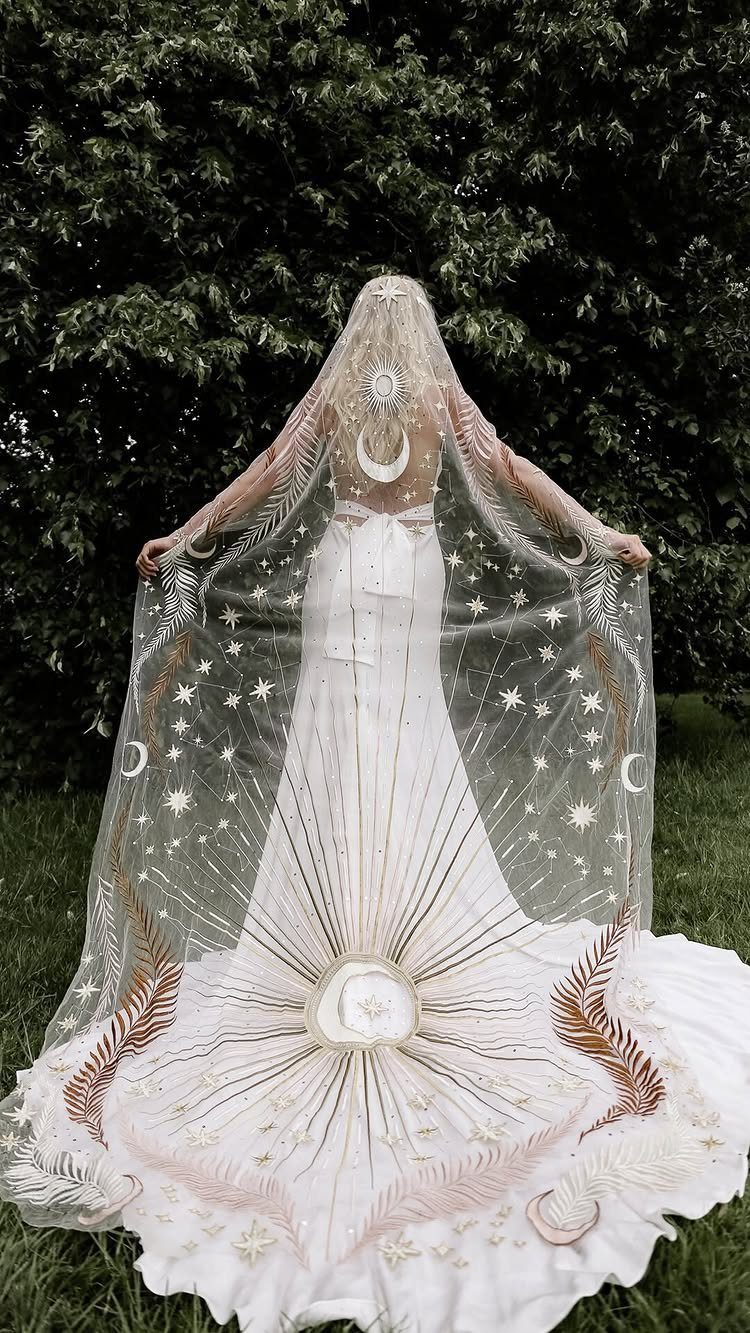 Goddess Wedding Dress Styles: 19 Ideas for 2026 10 Woman in white wedding gown wearing a celestial gold embroidered sheer cape outdoors.