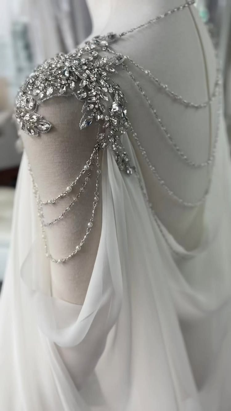 Goddess Wedding Dress Styles: 19 Ideas for 2026 12 White wedding dress with ornate crystal shoulder jewelry and draped rhinestone chains.