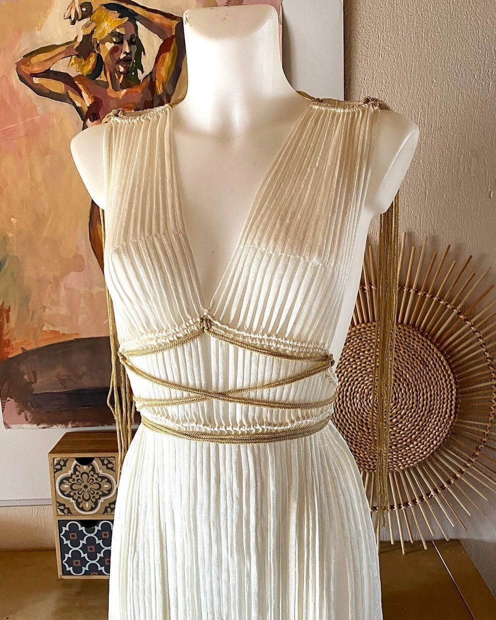 Goddess Wedding Dress Styles: 19 Ideas for 2026 3 White pleated Grecian dress on a mannequin with gold braided waist details.