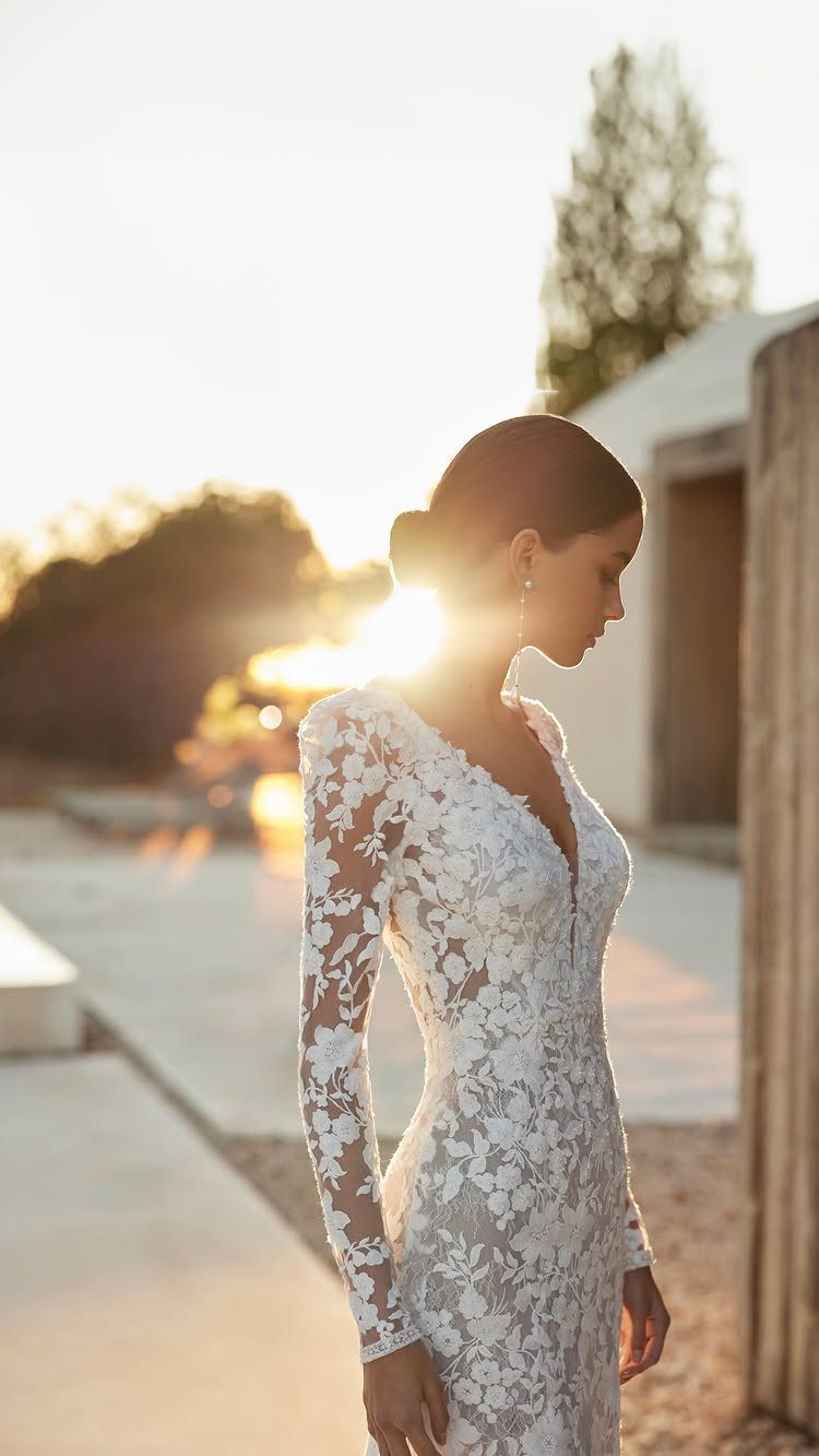 Goddess Wedding Dress Styles: 19 Ideas for 2026 9 Woman in a long-sleeved white lace wedding dress during a golden hour sunset.