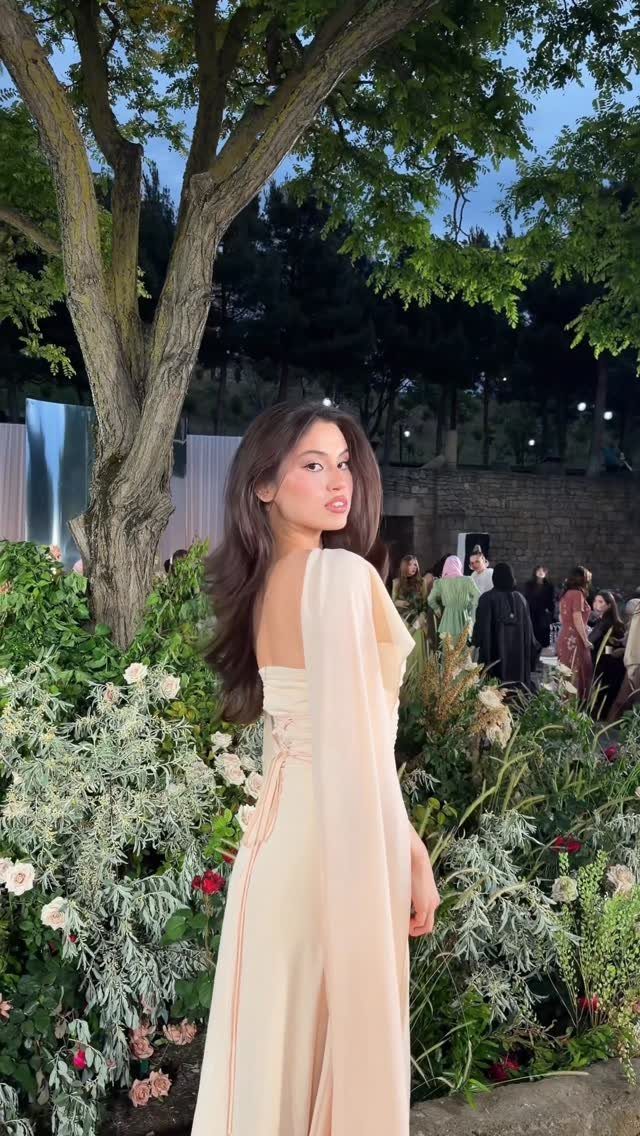 Goddess Wedding Dress Styles: 19 Ideas for 2026 16 Woman in a flowing cream goddess wedding dress standing by a tree and flowers.