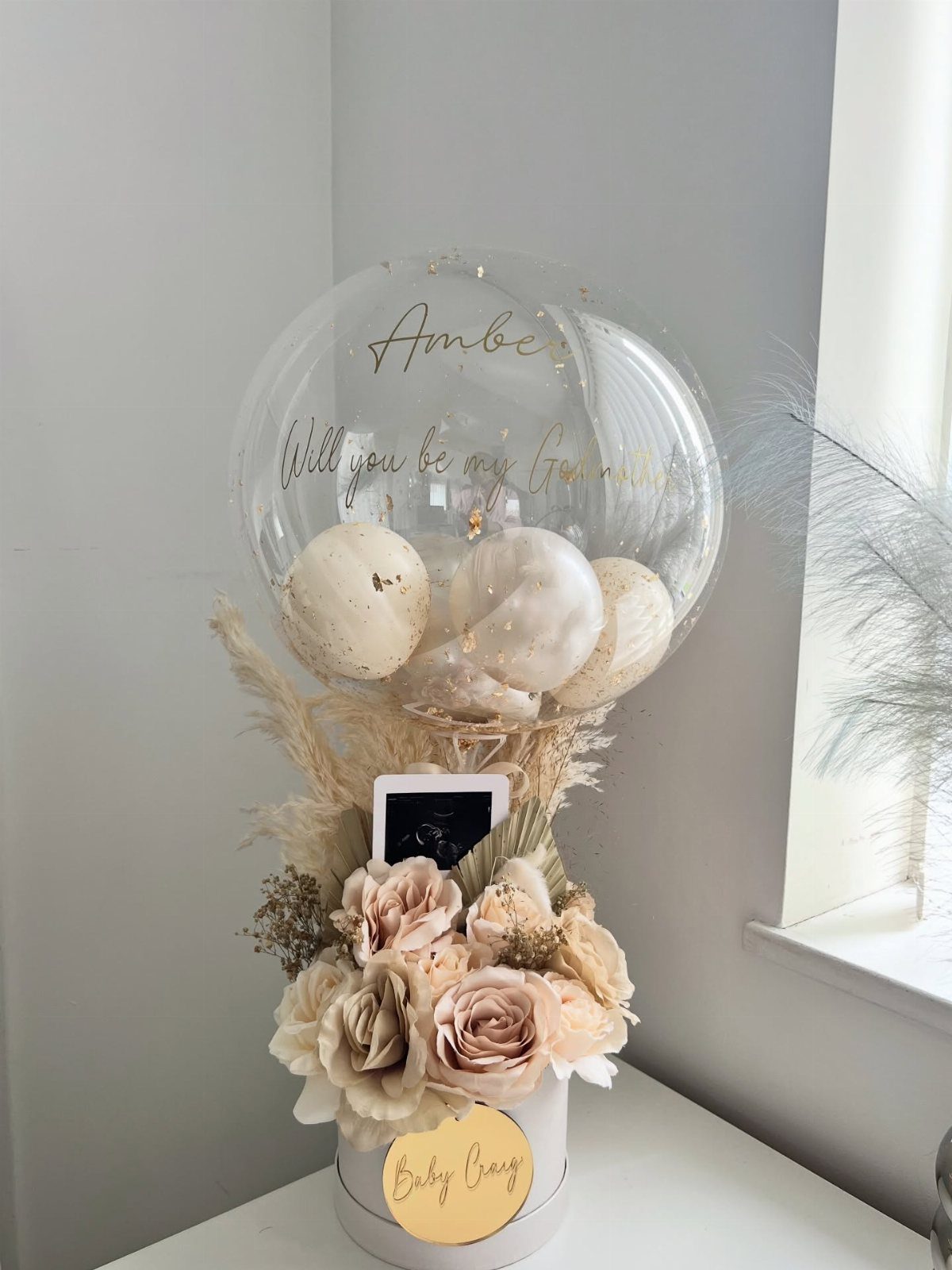 7 Godparent Proposal Box Ideas to Make the Ask Special 3 Godmother proposal gift box with beige roses, a polaroid photo, and a clear balloon.