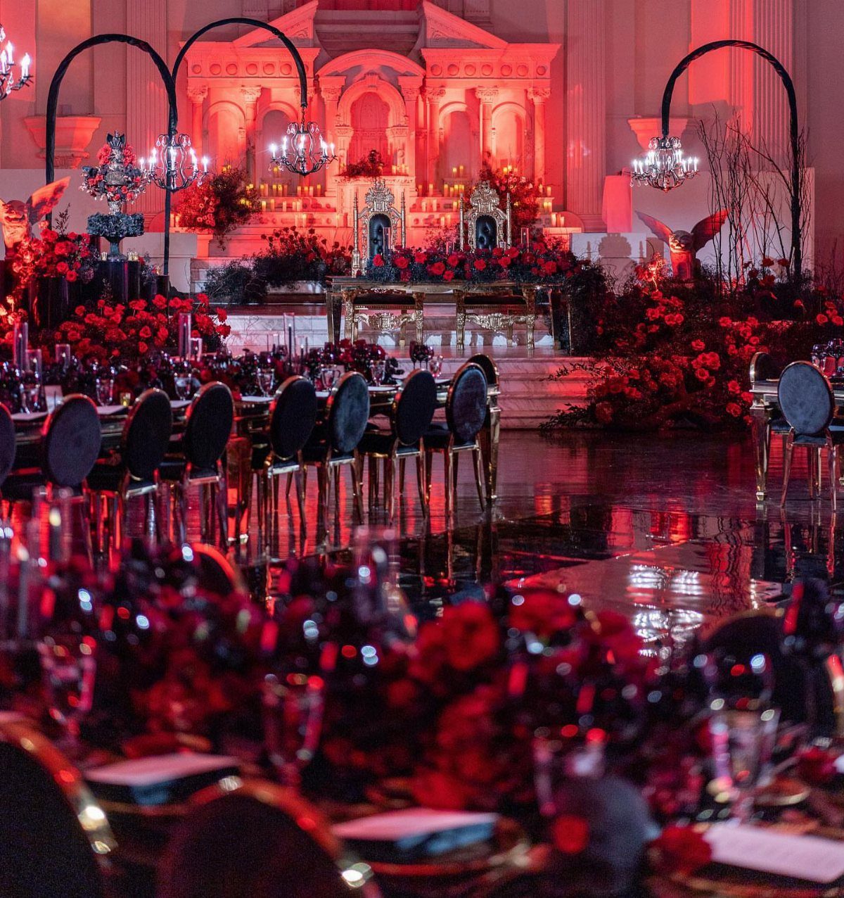 Red-lit wedding reception hall with black chairs and abundant red floral centerpieces.