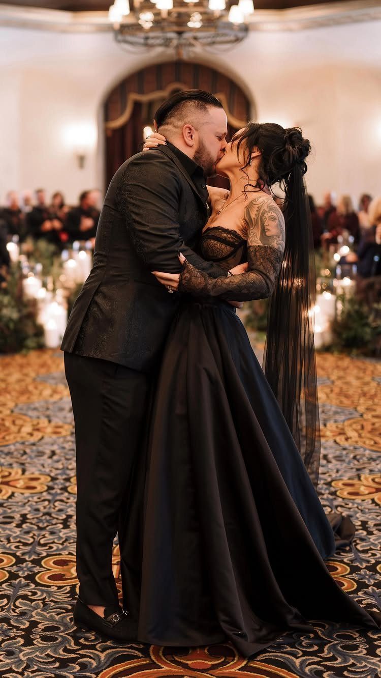 Couple kissing at a wedding, woman in a black gothic gown and long veil.