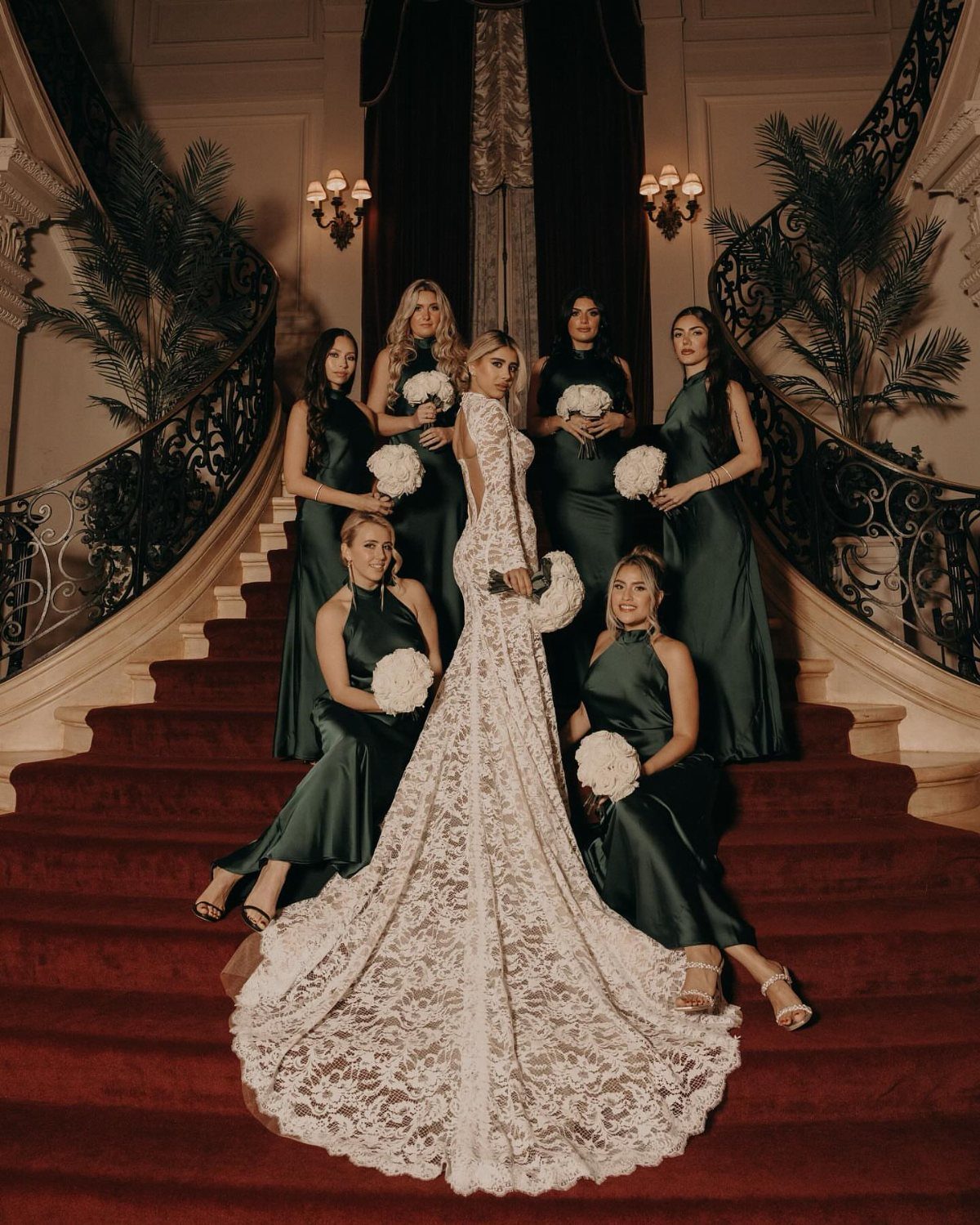 Bride in white lace gown with bridesmaids wearing dark green satin dresses.