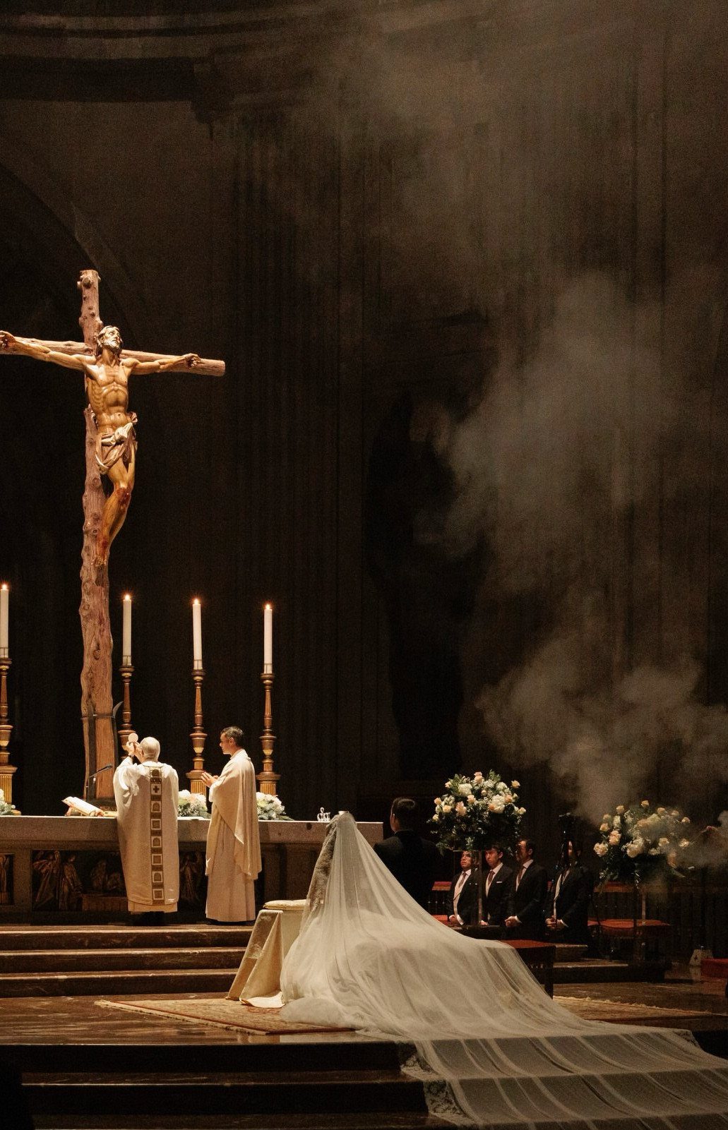 Bride kneeling at a church altar with a large crucifix and atmospheric fog.