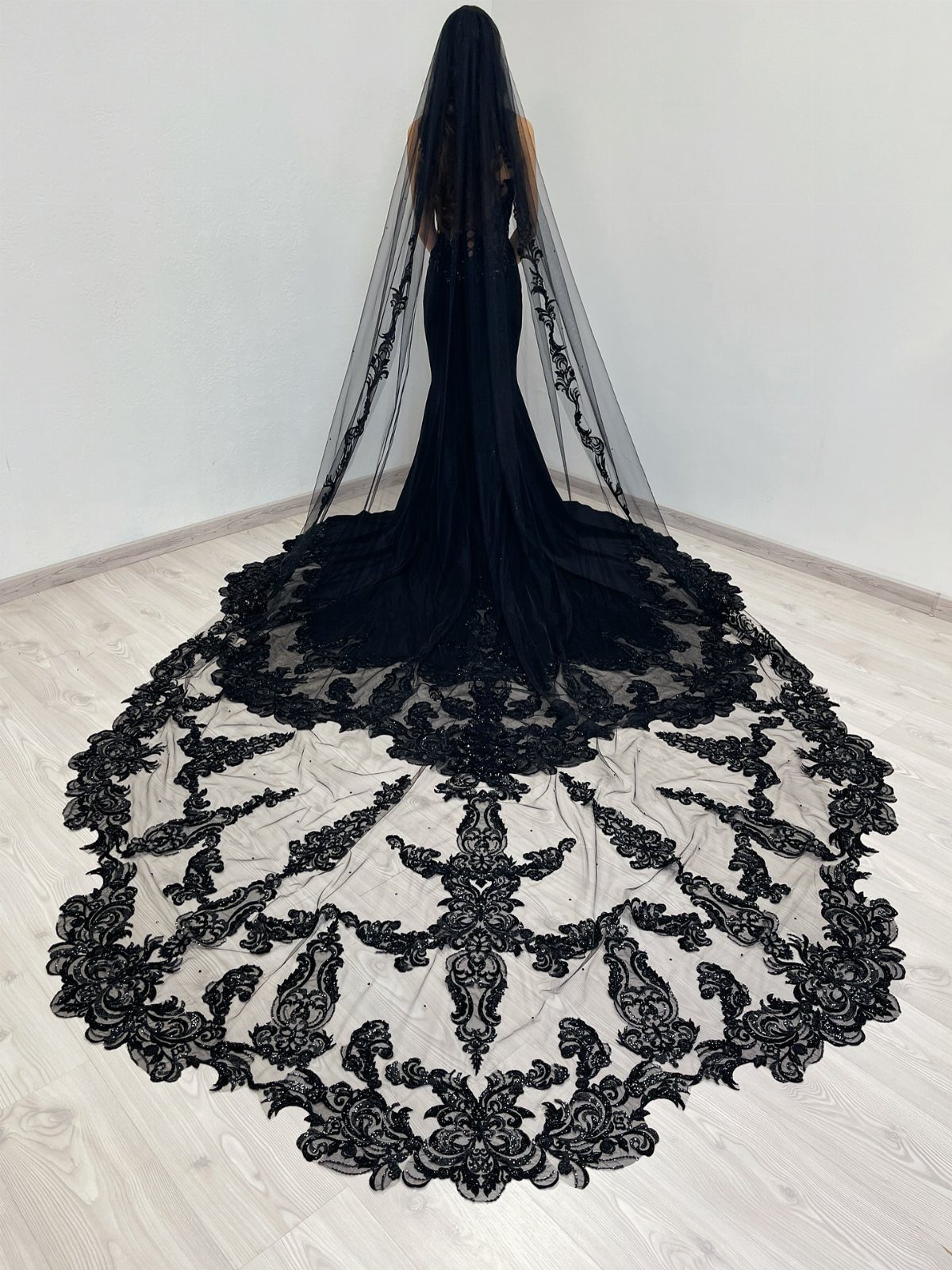 Black wedding gown with a long, intricate lace veil spreading across a wooden floor.