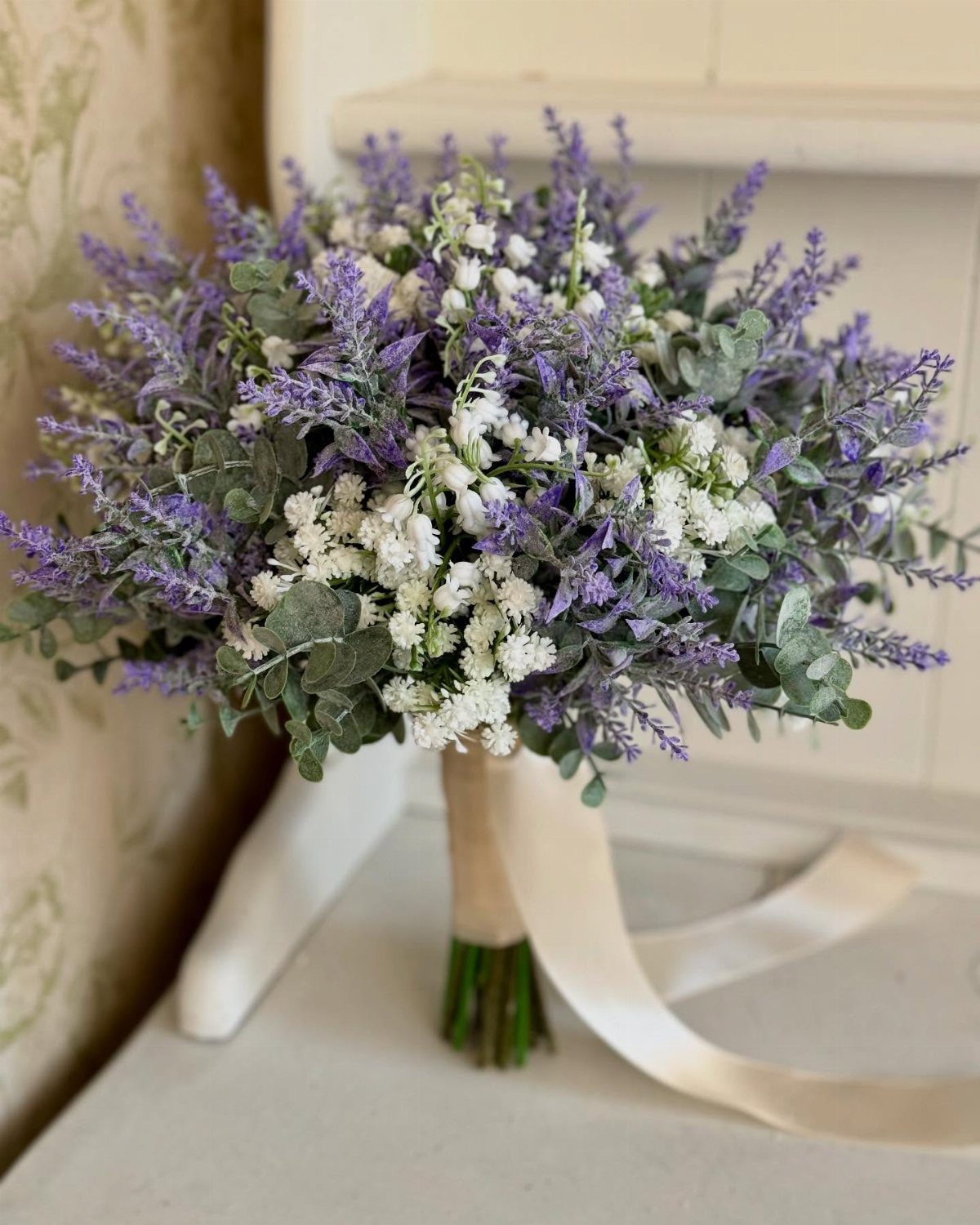 Bridal bouquet with purple flowers, white blossoms, and green eucalyptus tied with cream ribbon.