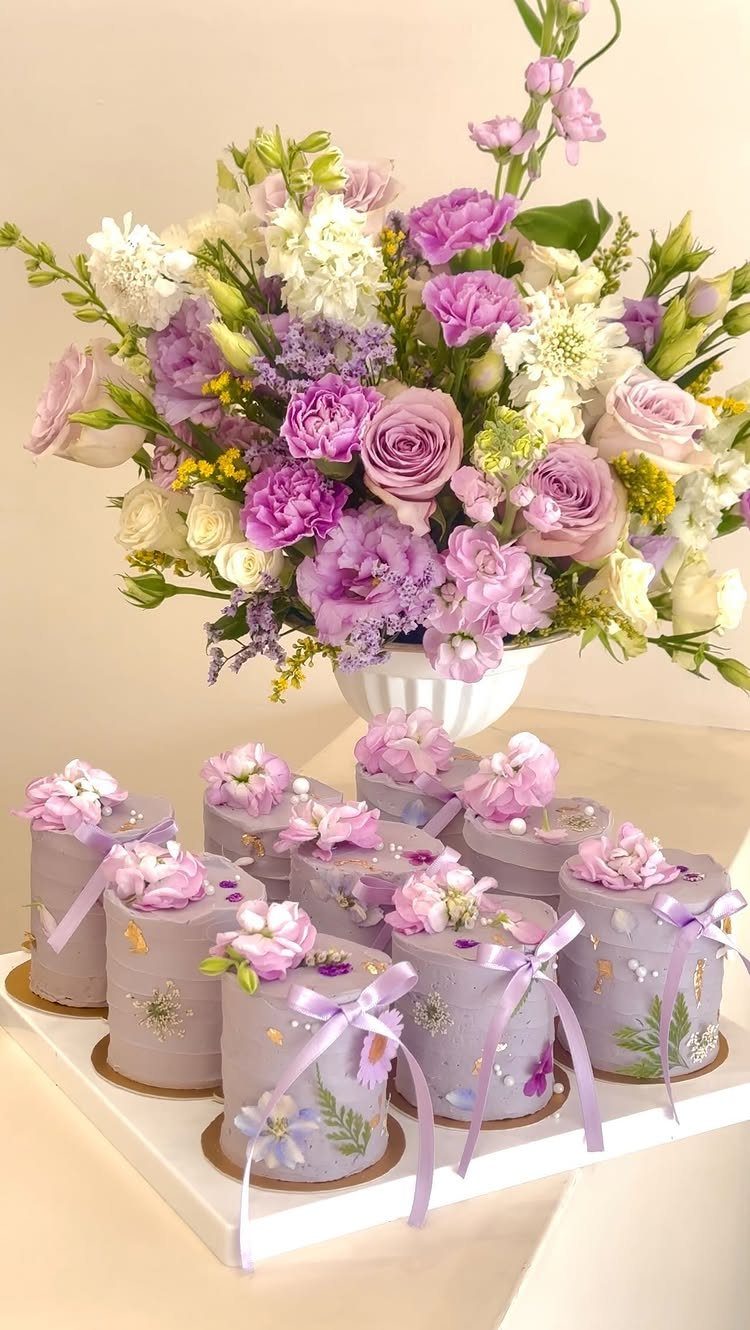 Small purple cakes with floral decorations and ribbons next to a large flower bouquet.