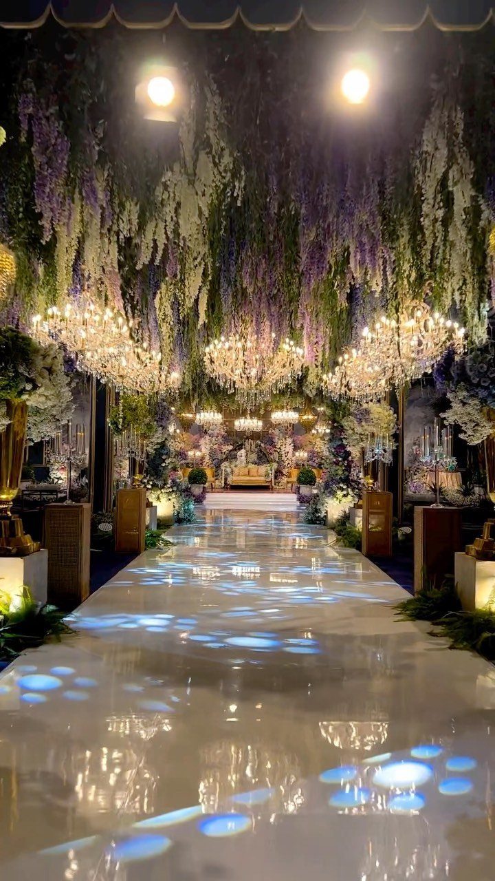 Wedding aisle with glossy white floors and hanging purple and green floral ceiling decorations.