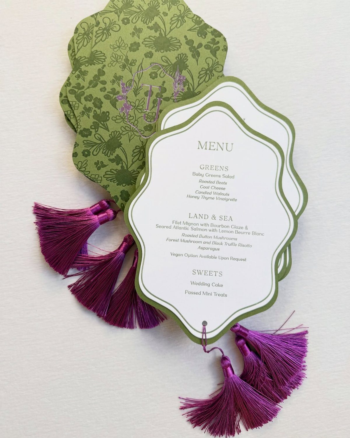 Wedding menu card with green border and purple tassels on floral paper.