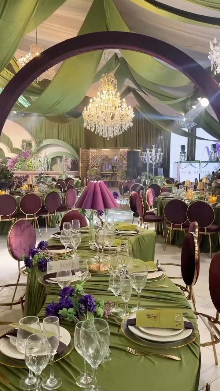 Green tablecloths and purple chairs with floral centerpieces in a decorated wedding venue.