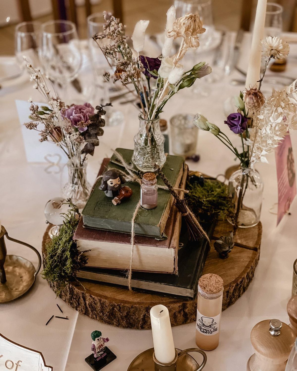 Vintage books stacked on a wood slice with small vases of purple flowers.