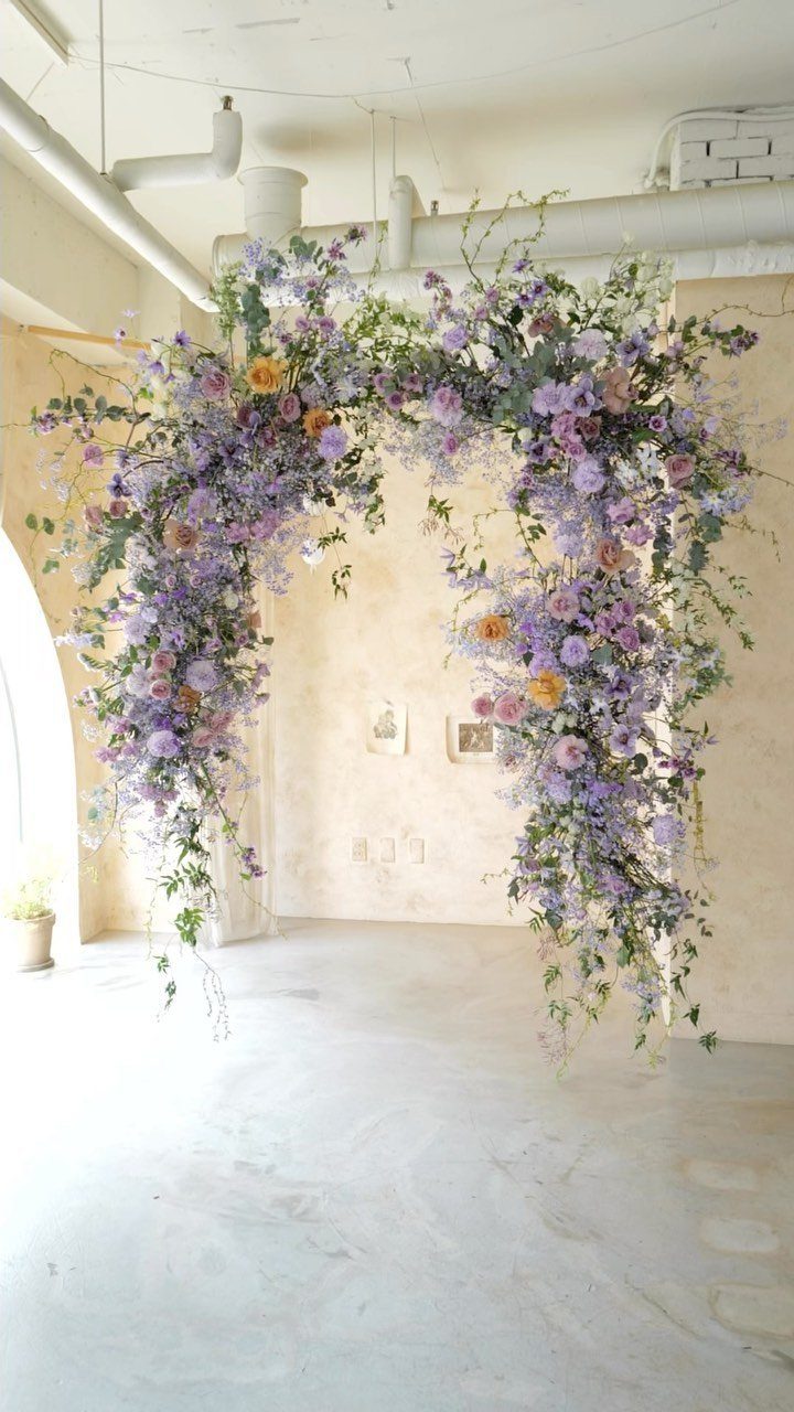 Floral wedding arch with purple and lavender flowers and green foliage indoors