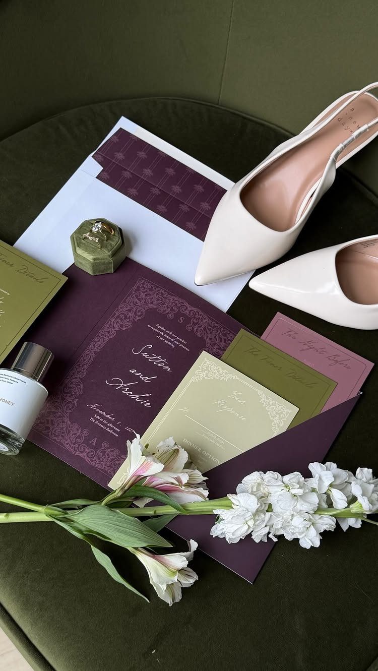 Wedding invitations in purple and olive green with nude heels and white flowers.