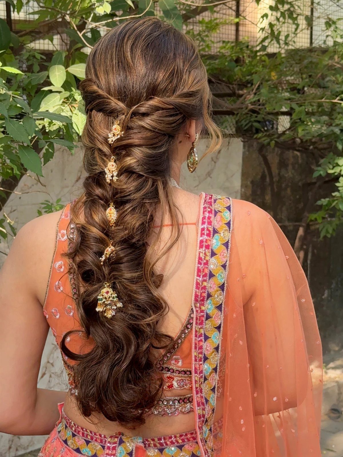 6 Hair Down Wedding Styles That Keep the Veil, the Volume, and the Vibe 6 Woman with long brown hair in an intricate braid decorated with gold floral ornaments.