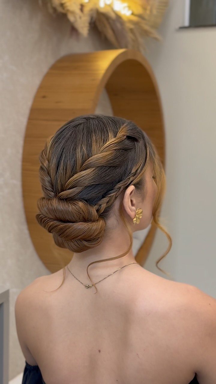 18 Hoco Updo Hairstyles From Braids to Sleek Buns 6 Woman with blonde-highlighted hair in an intricate braided low bun hairstyle.