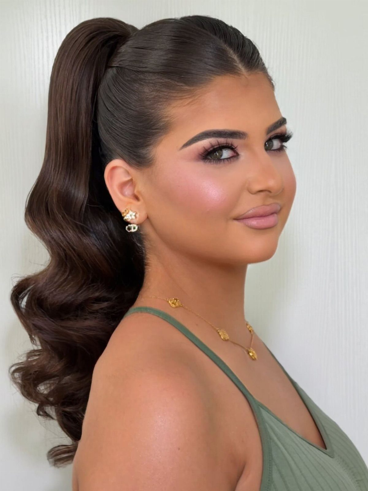 18 Hoco Updo Hairstyles From Braids to Sleek Buns 12 A young woman with dark hair styled in a sleek, wavy high ponytail.
