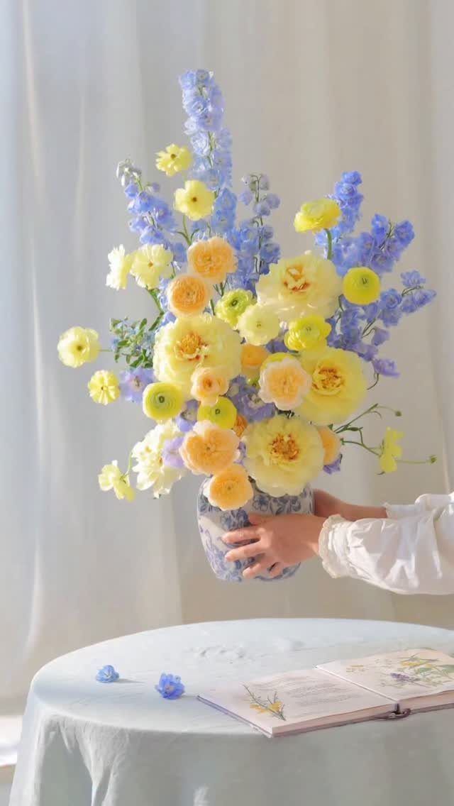 15 Ideas de Ramos de Flores for Every Table and Season 12 Yellow ranunculus and blue delphinium flowers in a ceramic vase held by hands.