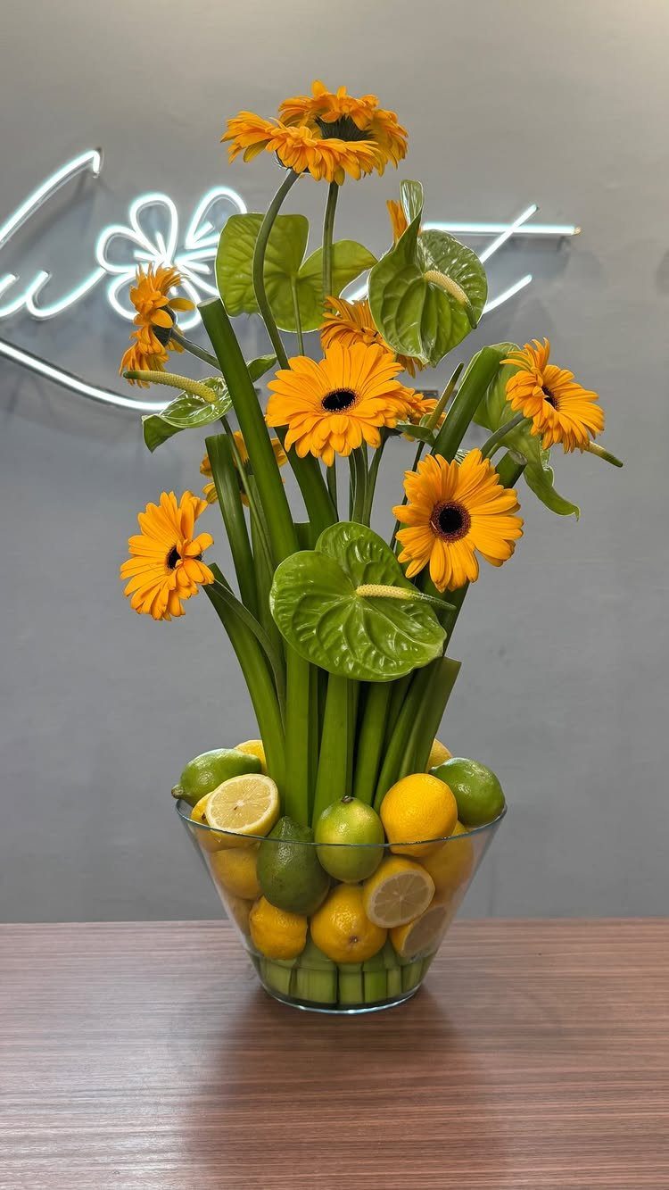 15 Ideas de Ramos de Flores for Every Table and Season 3 Yellow gerbera daisies and green anthuriums arranged in a bowl with citrus fruits.