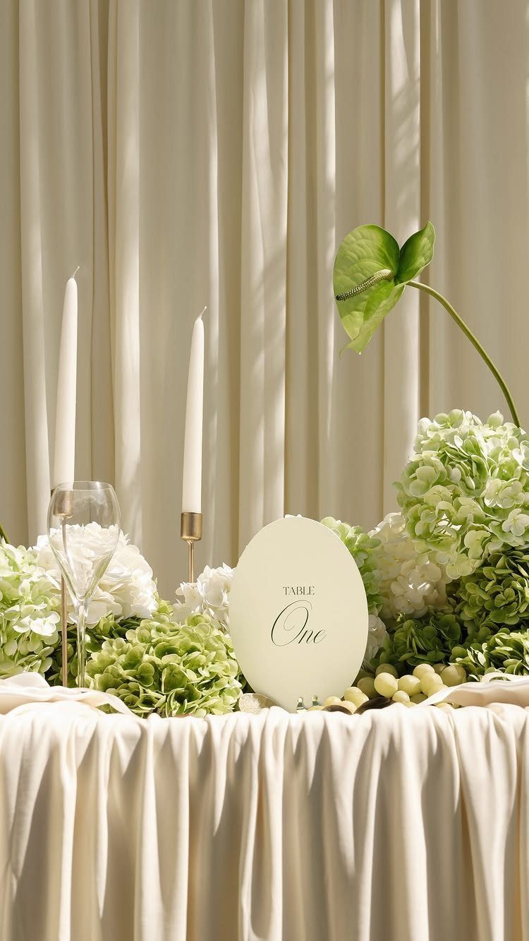 Ivory draped tablecloth with white and green hydrangeas and tall white taper candles.