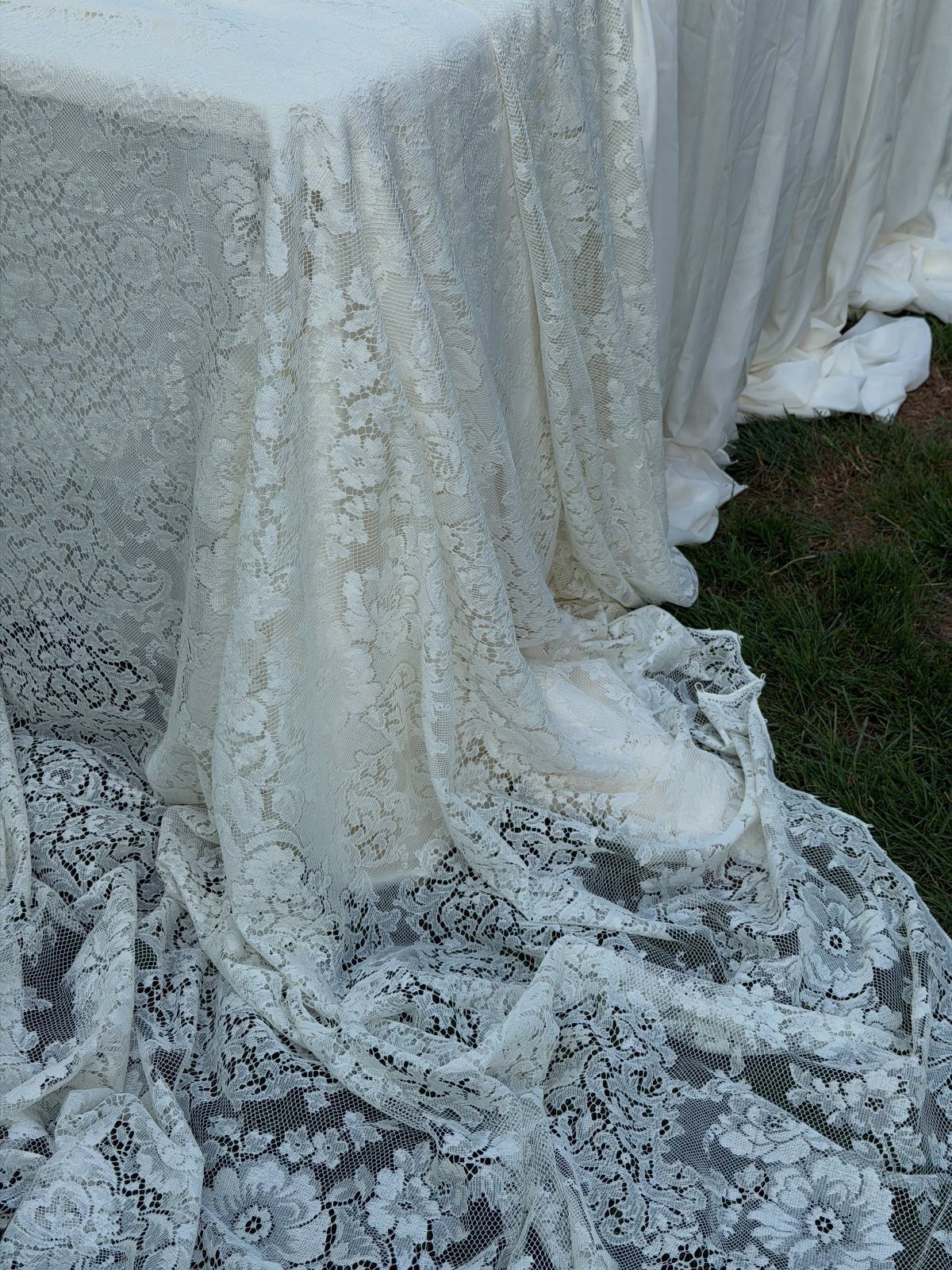 Ivory lace tablecloth with floral patterns draped over a table onto green grass.
