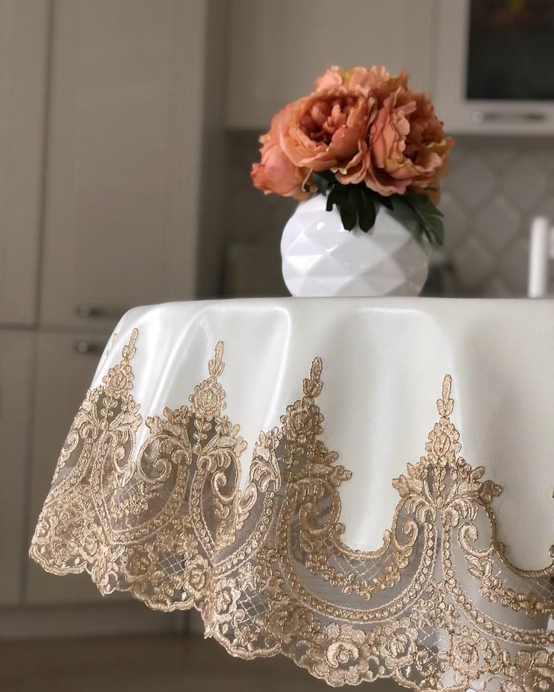 Ivory round tablecloth with gold lace embroidery and peach peonies in a vase.