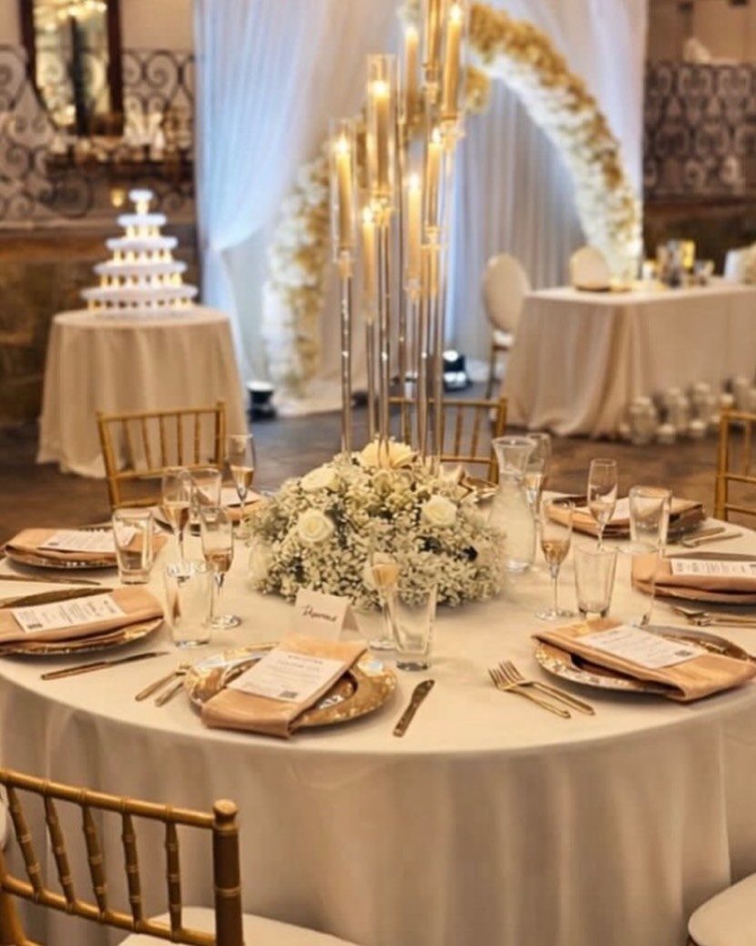 Round wedding table with ivory tablecloth, gold chargers, and tall gold candelabra centerpiece.