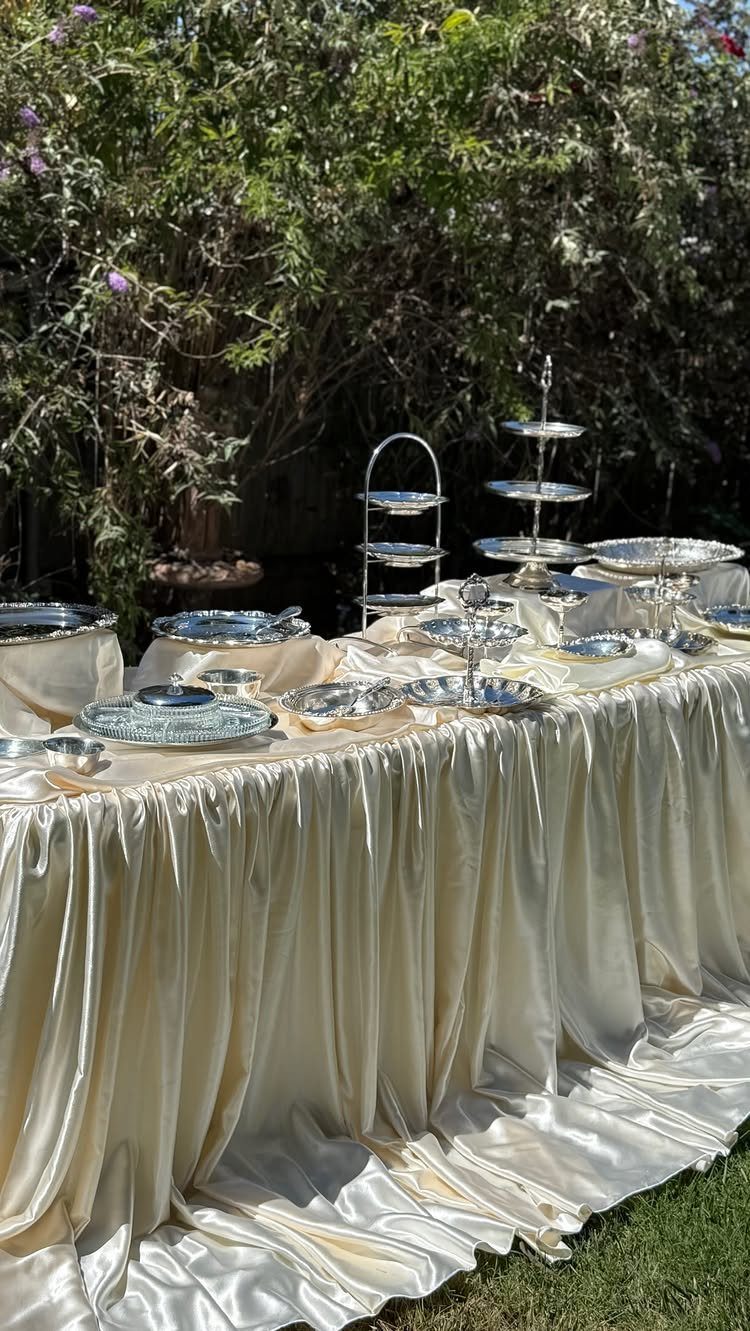 Ivory satin tablecloth on a buffet table with silver platters outdoors