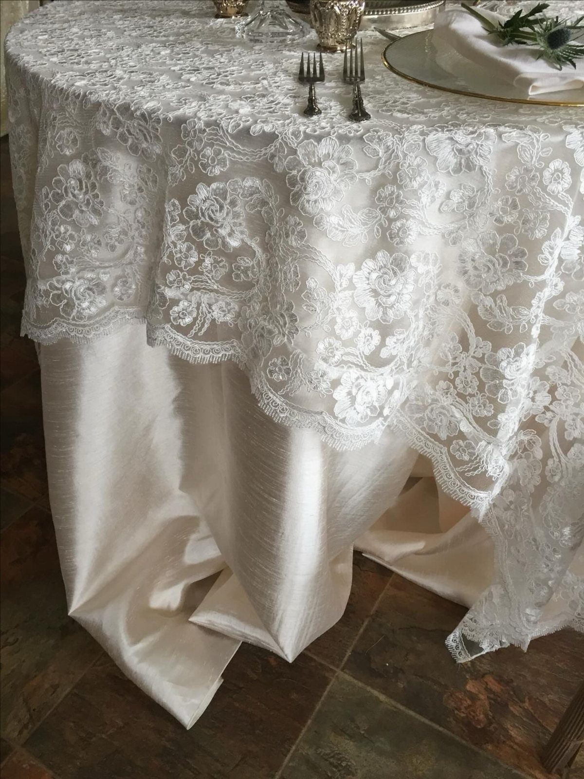 Ivory satin tablecloth with a white lace overlay on a round wedding table