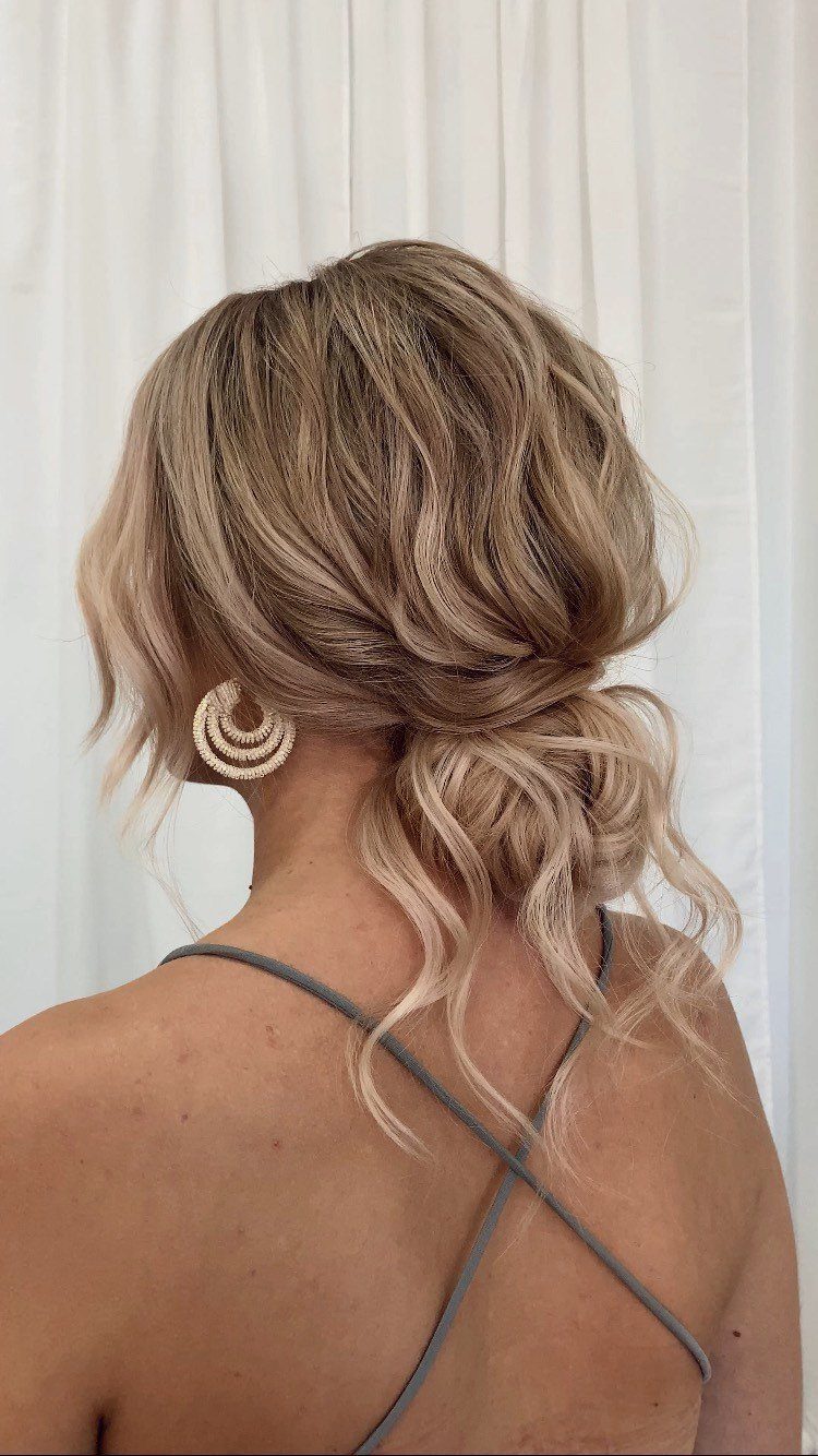 18 Low Messy Bun for Wedding Ideas with Braids and Florals 10 Blonde woman with a loose messy low bun and beaded hoop earrings.