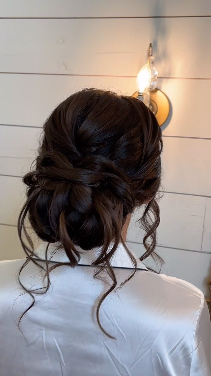 18 Low Messy Bun for Wedding Ideas with Braids and Florals 15 Low messy bun with curly tendrils on dark brown hair wearing white satin.